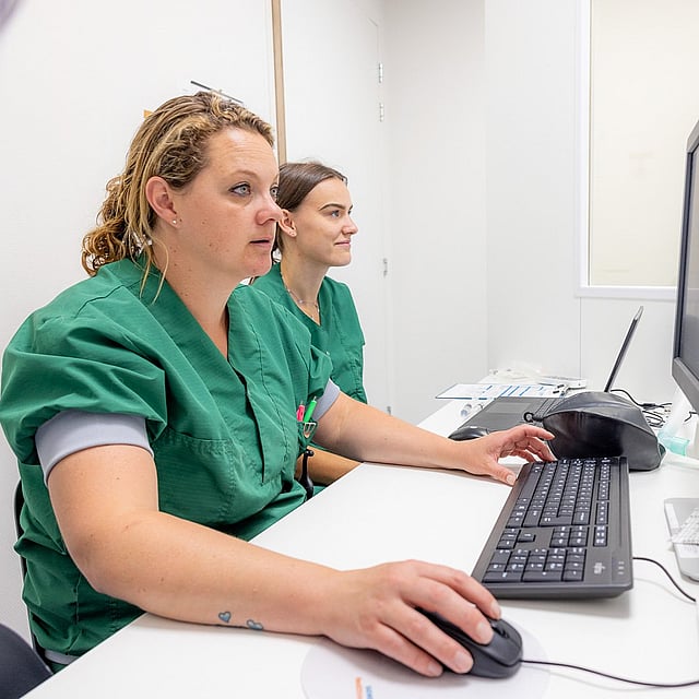 Een groep vrouwen in scrubs zittend aan een bureau met een computer.