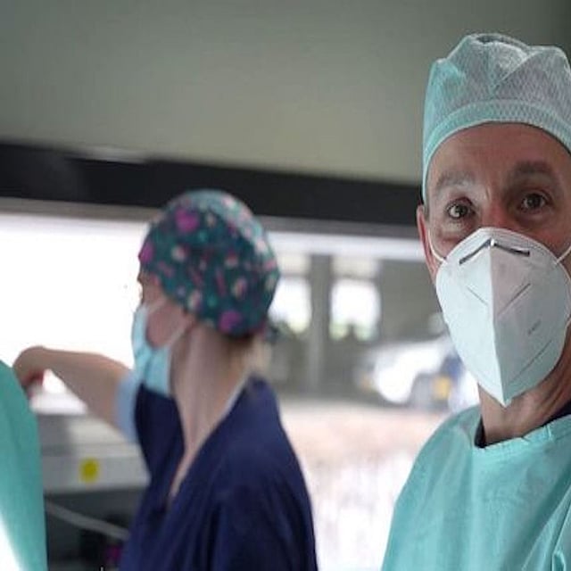 Een persoon die chirurgische scrubs en gezichtsmasker draagt.