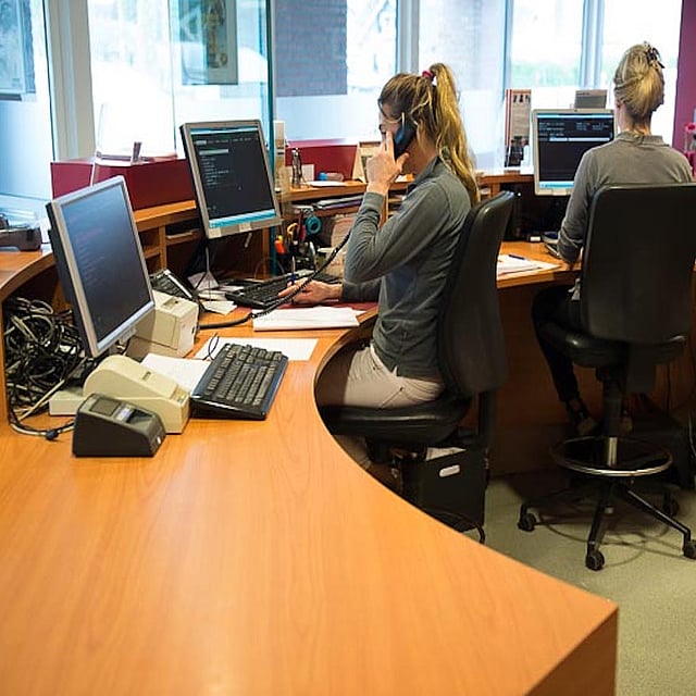 Een persoon die aan een bureau zit met haar telefoon.
