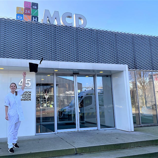 Een persoon in witte jumpsuit die voor een gebouw springt.