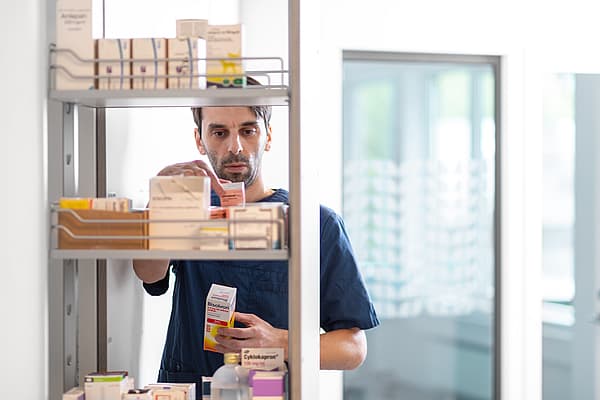 Een persoon die zich voor een plank met medicijnen bevindt.