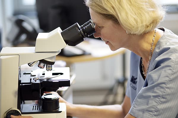 Een persoon die door een microscoop kijkt.