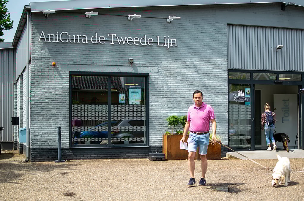 Een persoon die met een hond aan de lijn buiten een gebouw loopt.