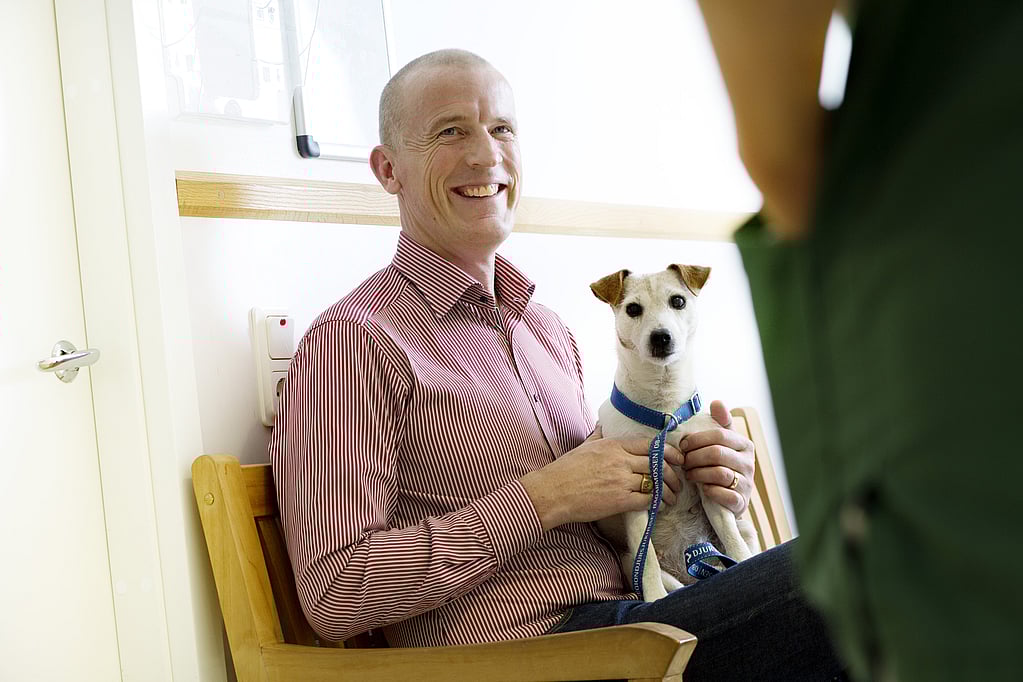 Een persoon die in een stoel zit en een hond vasthoudt.
